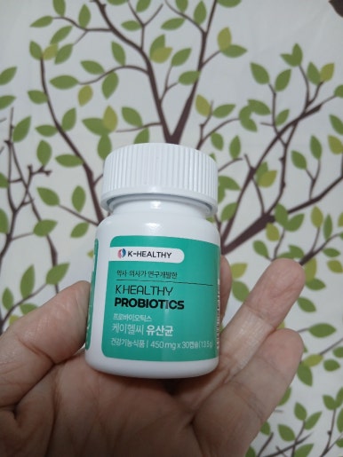 약사가 설계하여 콜레스테롤 수치 낮추는 방법에 도움을 주는 케이헬씨 유산균-약사·의사가 연구개발한' 문구가 선명한 유산균 제품을 손에 들고 있어 진정성 있는 내돈내산 후기임을 강조합니다.