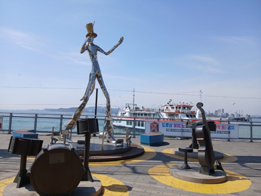 인천 월미문화의거리 야외 공연장 인근의 악기 조형물과 푸른 인천 앞바다-인천 월미바다열차에서 내려 벚꽃길을 따라 걷다 보면 만날 수 있는 월미문화의거리 풍경입니다. 탁 트인 바다와 예술적인 조형물이 여행의 즐거움을 더해줍니다.