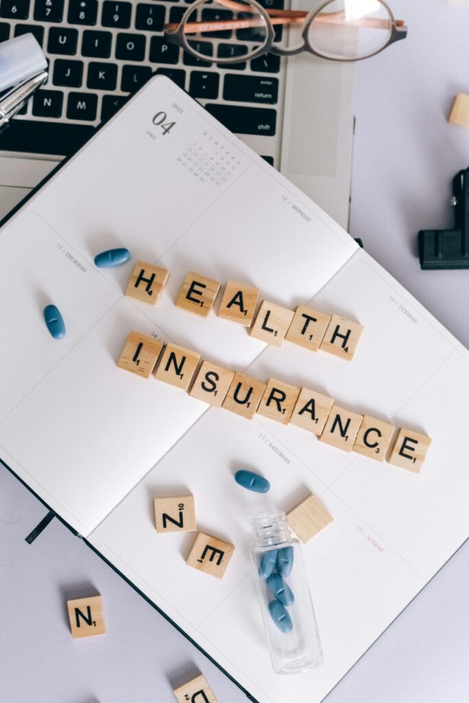 고유가 지원금 2차 기준 선정을 위한 건강보험료 합산 및 가구원 수 확인 이미지-다이어리 위에 'HEALTH INSURANCE'라는 글자가 놓여 있어, 지원금 선정의 핵심인 건강보험료 산정 방식을 시각적으로 보여줍니다.